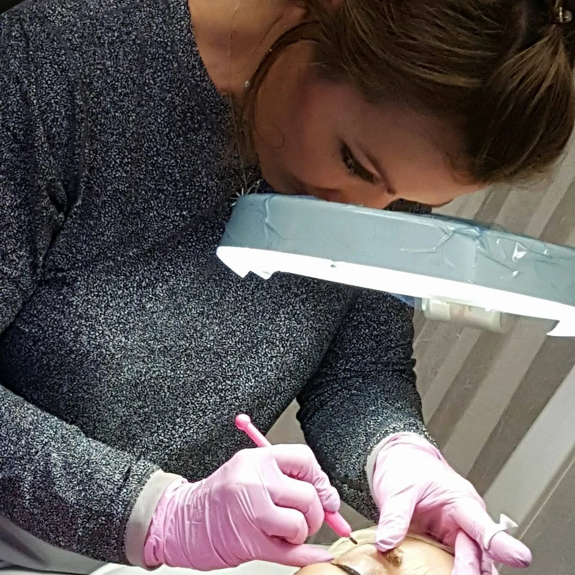 A person wearing pink gloves uses a tool on another person's skin under a magnifying light, exemplifying the meticulous care typical of luxury skincare treatments.