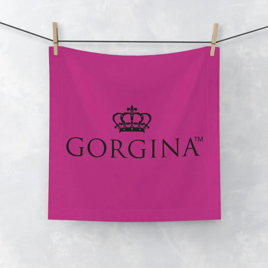 A Face Towel in pink, featuring a crown logo and the text "GORGINA™," is hanging on a clothesline against a light background.