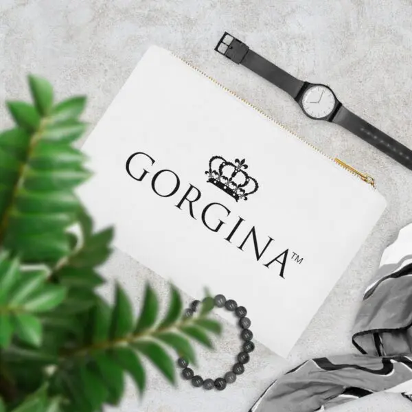 A Cosmetic Bag featuring "GORGINA" and a crown logo, displayed alongside a watch, green leaves, a necklace, and a black-and-white striped scarf on a gray surface.